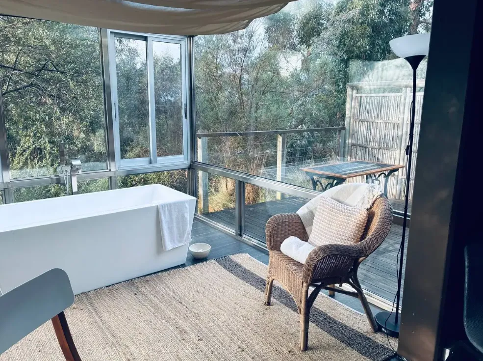 Freestanding bath and wicker chair in the glass atrium overlooking the bush