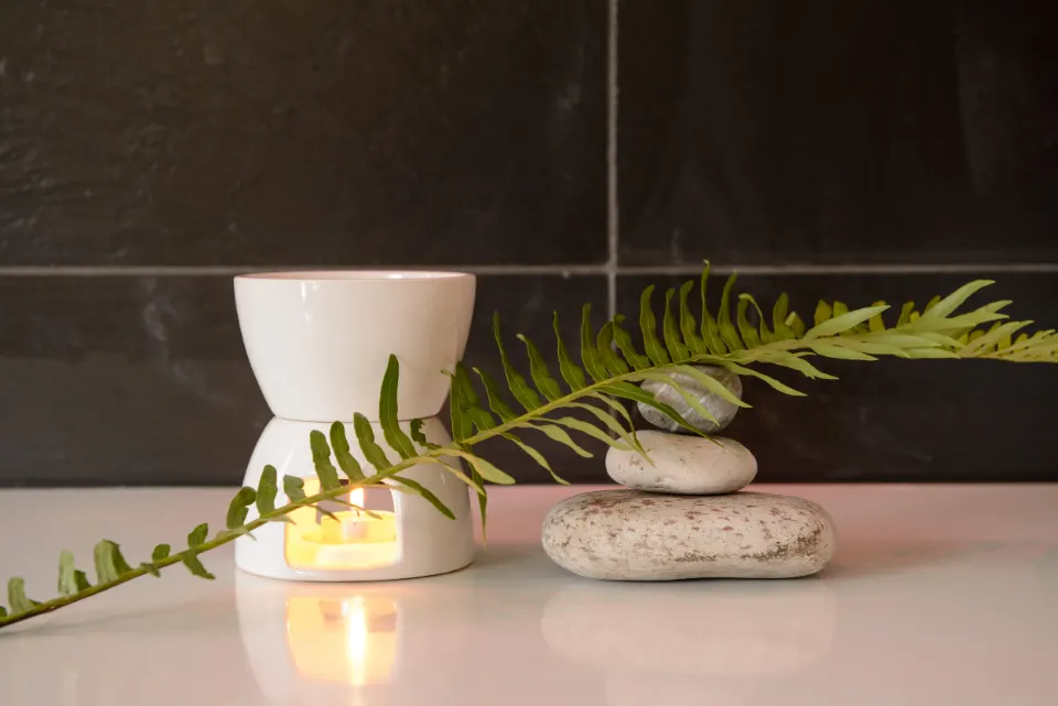 Candle-lit oil burner beside stacked stones and a fern